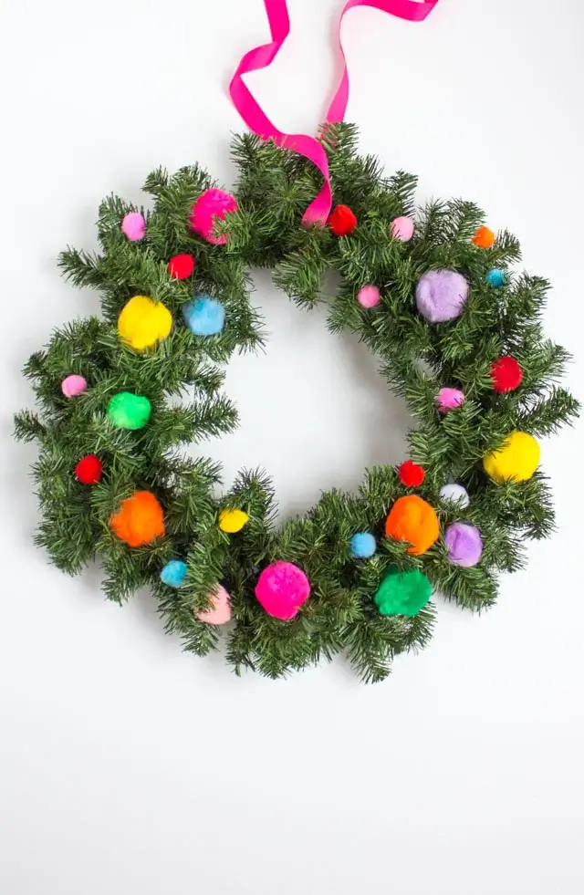 A fun and colorful DIY Christmas decorations project: a green evergreen wreath adorned with clusters of bright red and white pom poms.