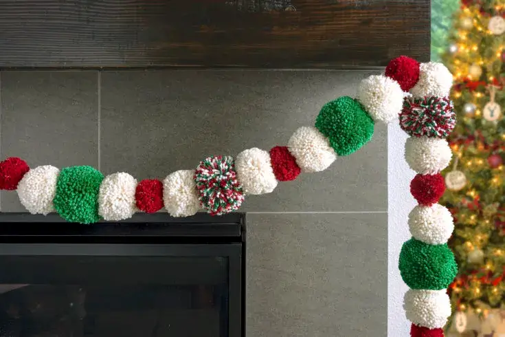  A vibrant and colorful pom-pom garland in red, white, and green, draped on a mantle as fun and textural holiday home decor.