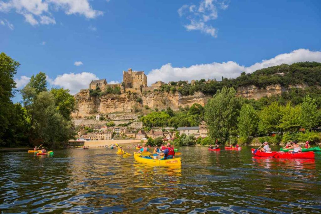 People kayaking on the serene Dordogne river, a classic slow travel activity past a cliff-side village