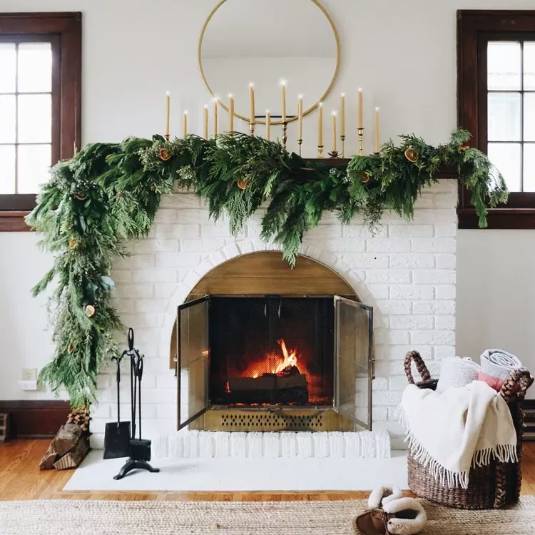  A minimalist Christmas decoration featuring a mantel draped with a green garland and a row of white candles.