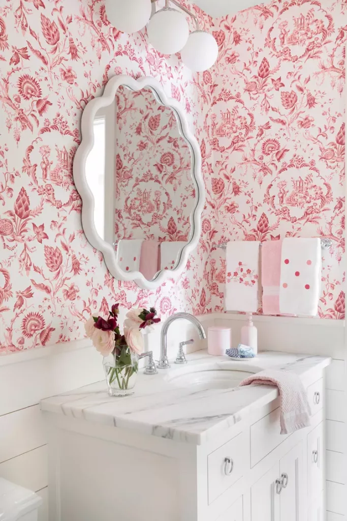 A funky bathroom featuring bright pink wallpaper and art deco-inspired mirrors and globe lights