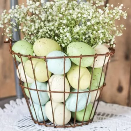 Rustic wire Easter basket filled with pastel-speckled eggs and baby’s breath flowers, creating a simple yet beautiful Easter centerpiece for the coffee table.