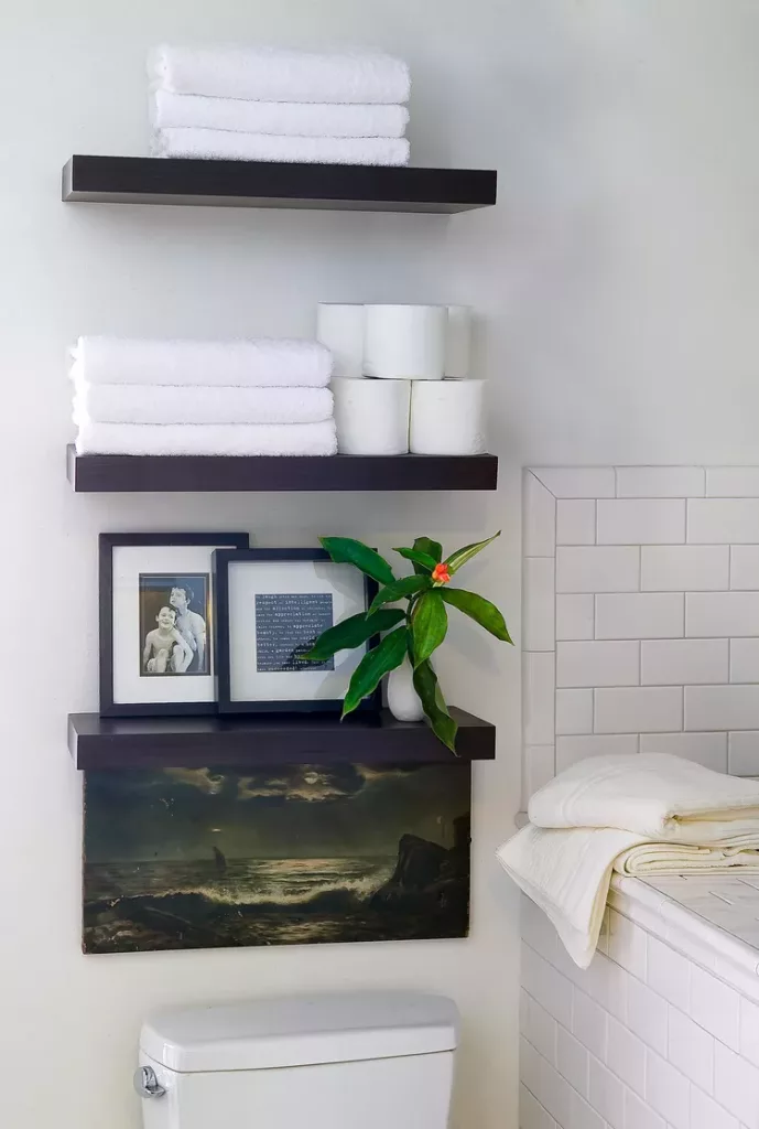 floating shelves about toilet with deor and framed art