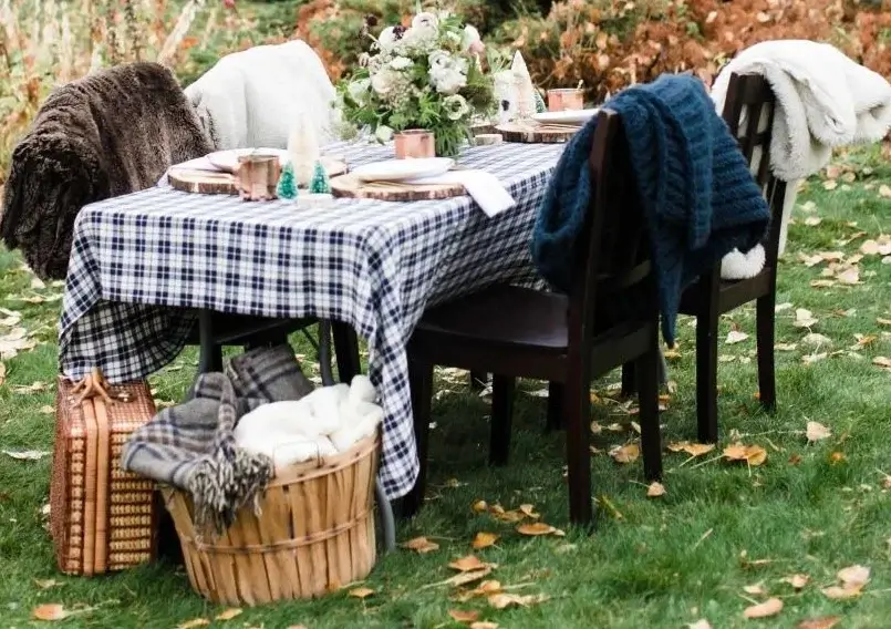 A long rustic table set for a winter gathering, complete with blankets on every chair and warm, ambient lighting.