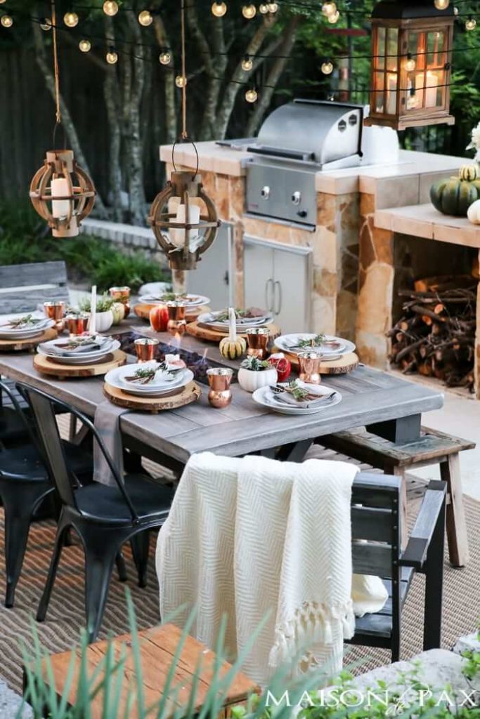 A rustic table with a built-in fire pit, enjoying a meal with wood charger plates and candlelight.