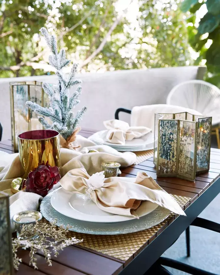 A festive Christmas lunch setting on a balcony table with aged glass lanterns and blankets draped over the chairs.