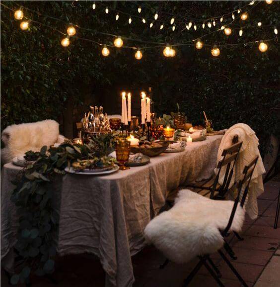 A collection of handcrafted, imperfect stoneware plates and bowls under the soft glow of string lights on a cozy table.