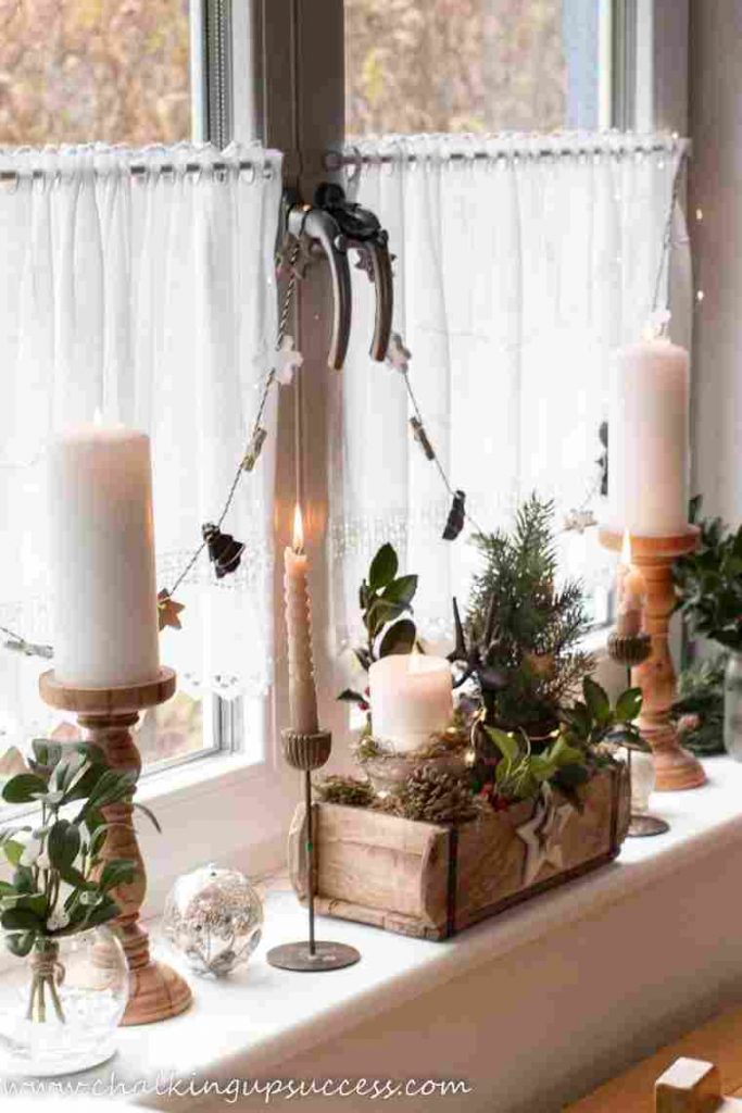 A window sill display with varying height candles and spruce greenery in a minimalist Christmas home.