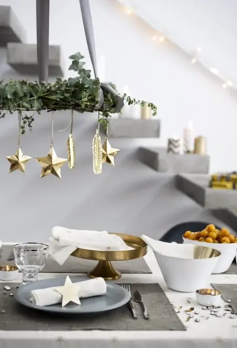 A hanging mobile with evergreens and minimalist christmas ornaments above a dining table.
