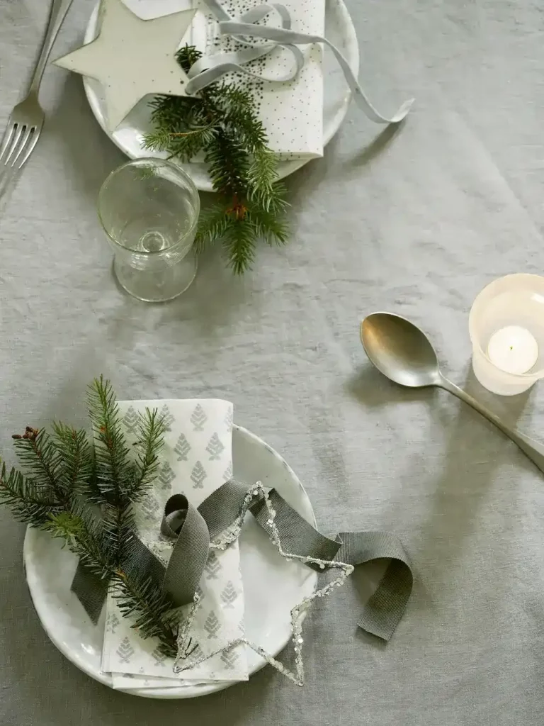 A neutral place setting with a sage green napkin and an evergreen sprig for a modern holiday home.