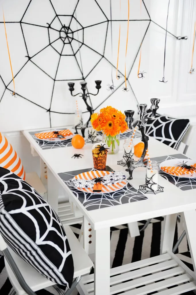Cozy Halloween festive table decor in a small apartment with a yarn spiderweb on the wall and orange accents for a holiday party.