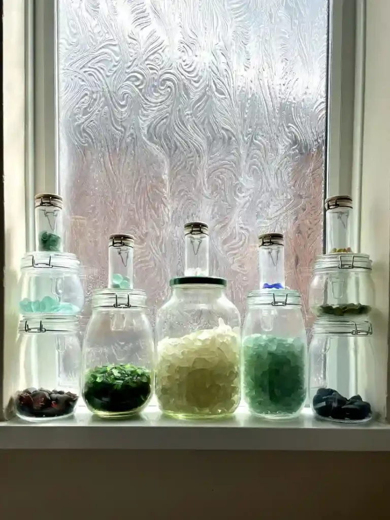 Colorful sea glass sorted in jars on a windowsill, a beautiful display for a foraged home