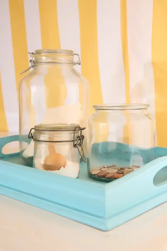 Apothecary glass canisters and vintage bottles styled as thrift store laundry decor for dry detergent storage.