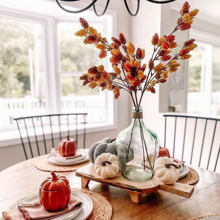 Simple fall table centerpiece with dried branches, foliage, and small pumpkins