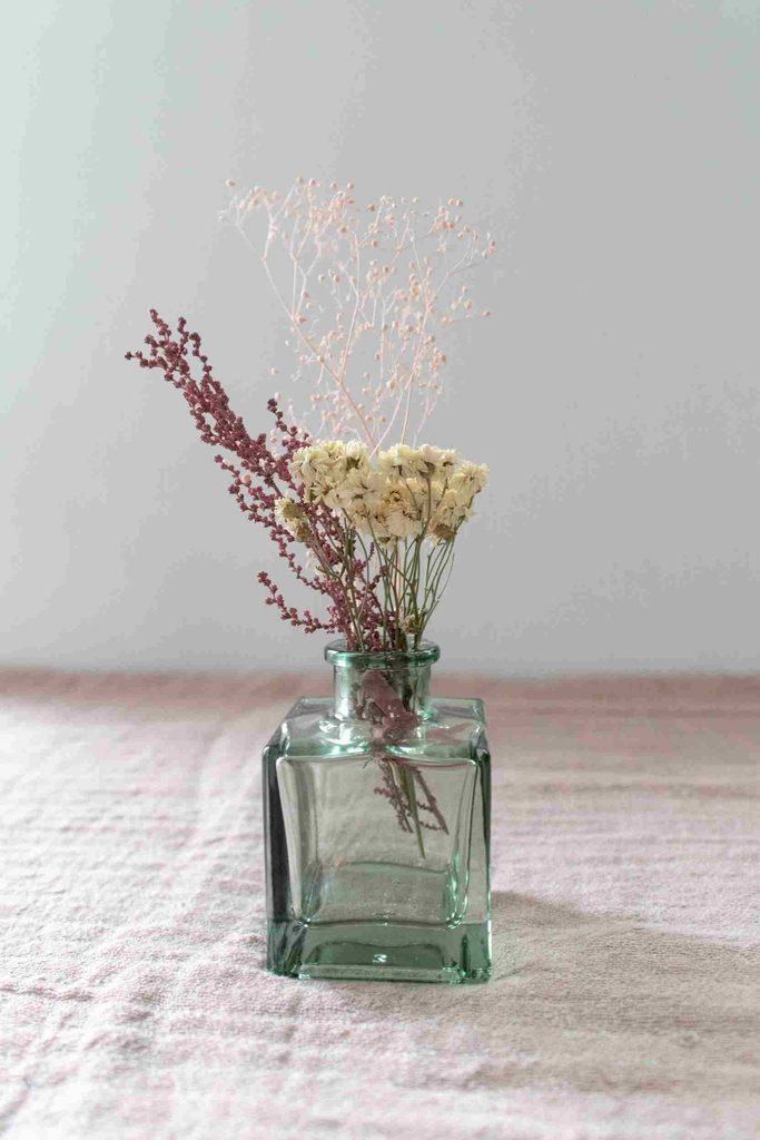 Small bud vase with dried flowers on a minimalist tablecloth