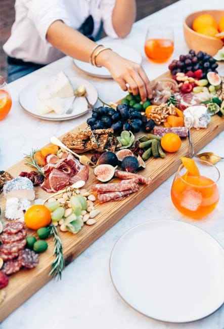 Wooden serving board with bread, cheese, fruit, meats, and nuts as Thanksgiving table decor